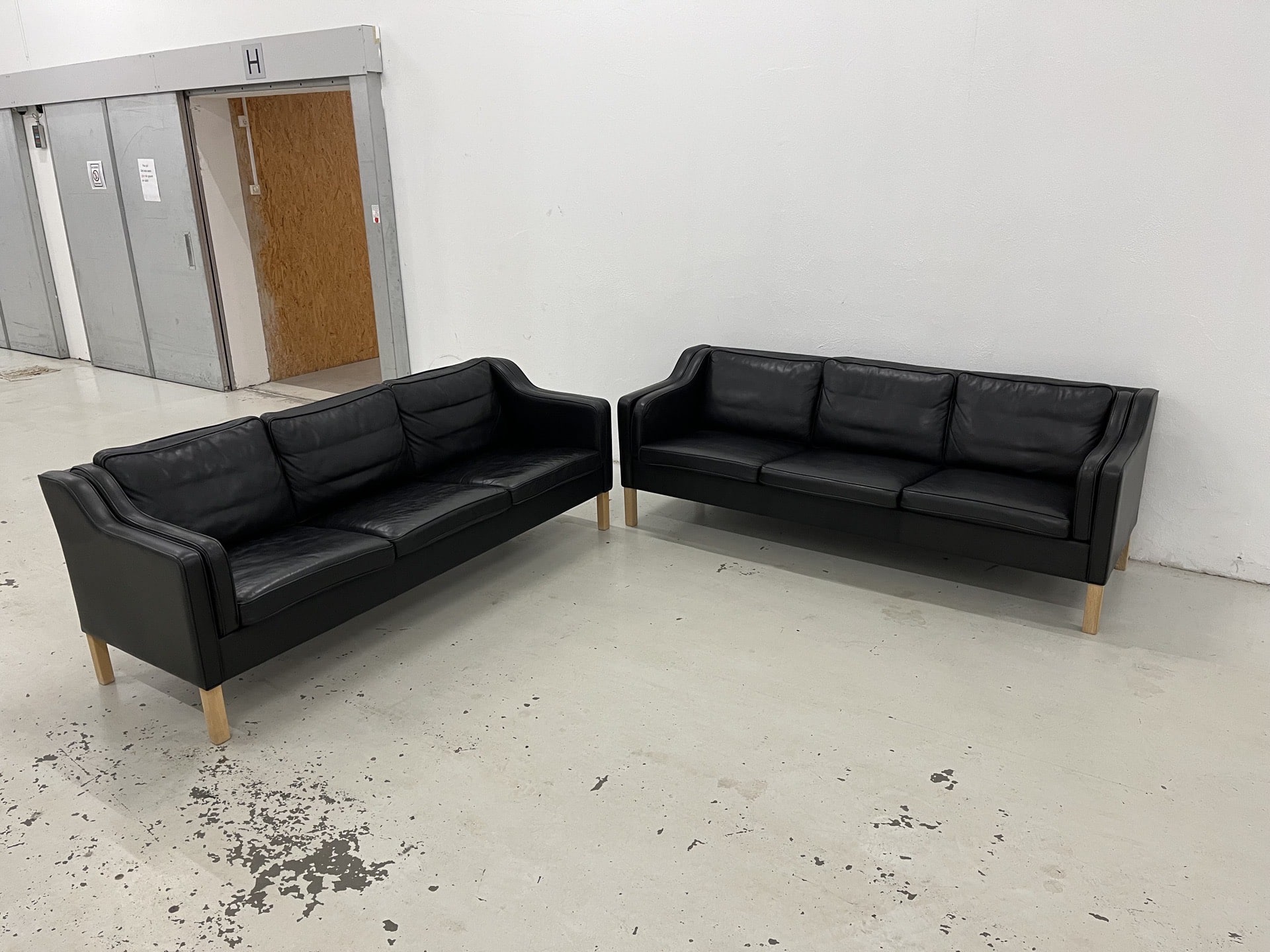 Mogens Hansen MH195 – Sofasæt bestående af 2x3personers sofaer i sort premium-læder med ben i lys eg. Pris: 36.000 kr.